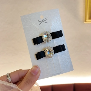 Elegant pair of black bow hair clips with oval rhinestones on a white card display
