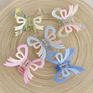 French cream acetate bow hair claws in five soft colors on a wooden tray
