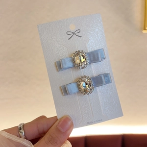 Close-up of grey-blue bow hairpins with oval rhinestones on a white display card