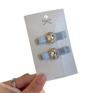 Pair of light blue silk bow hair clips with oval rhinestones on display card