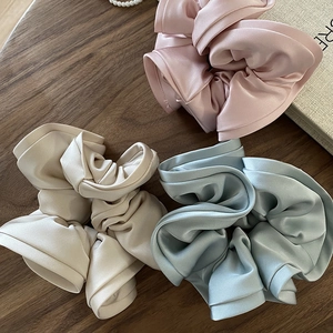 Close-up of three satin scrunchies in pastel pink, beige and blue on a wooden desk