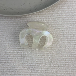 Dettaglio della pinza per capelli color crema perlato con riflessi arcobaleno e logo oro