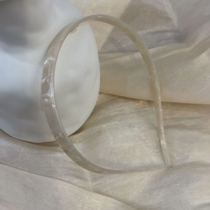 Detail view of cream marble pattern acetate headband on a white plaster statue