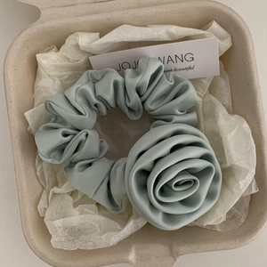 Close-up of a mint green satin scrunchie with a large handmade fabric rose in a gift box