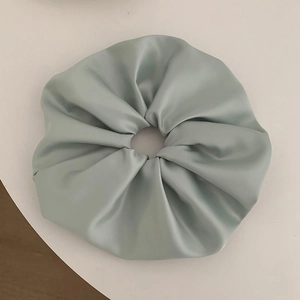Detail of a large mint green satin scrunchie with soft folds and glossy texture