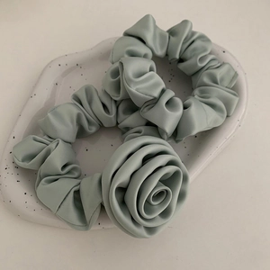 Sage green scrunchie set with large fabric flower on a white ceramic tray