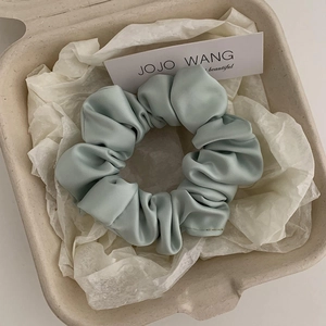 Detail shot of a soft mint green satin scrunchie placed in a premium gift box