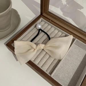 Detail eines eleganten beigen Organza-Bogen-Haargummis mit Perle in Vintage-Box