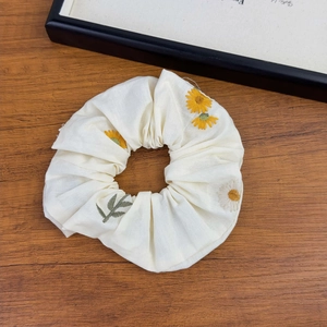 Detailed macro view of white fabric scrunchie with yellow daisy floral embroidery
