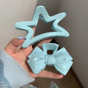 Close-up of star and bow shaped light blue hair claws held in hand for detail