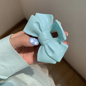 Detailed close-up of a light blue bow-shaped hair claw clip held by hand for sizing