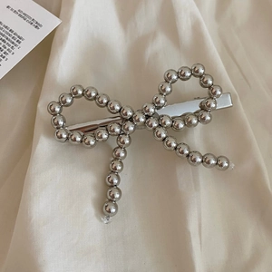 Barrette à cheveux nœud en perles argentées avec pendentifs sur fond en tissu beige