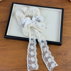 Detail of a creamy white lace scrunchie with floral bow streamers in a wooden setting