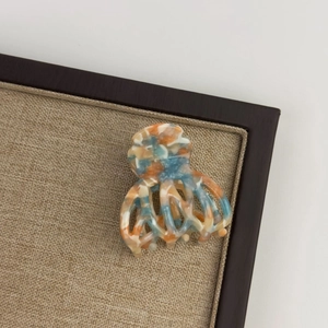 Top view of medium acetate hair claw clip with colorful marble pattern on a display tray