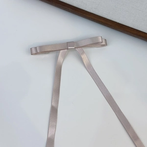 Detailed view of the elegant satin bow hair clip with long ribbons in soft champagne pink