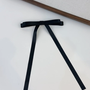 Detail of elegant black satin bow hair clip with long ribbon streamers on white background