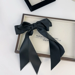 Elegant large black satin bow hair clip with long ribbons on a decorative cream tray