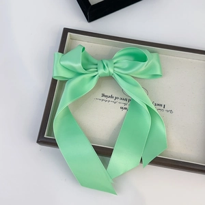 Close-up of mint green satin bow hair clip with long ribbons on wooden tray