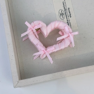 Detailed view of pink ribbon bows and satin heart hair claw on a beige tray