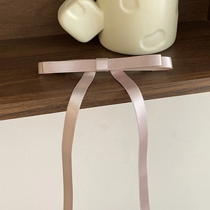 Macro detail of elegant satin bow hair clip with long ribbons in soft dusty rose pink