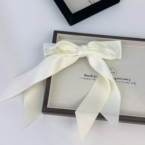 Macro shot of large cream satin double bow hairclip with long ribbons on a display tray