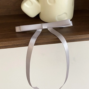 Close-up of a silver-grey satin bow hair clip with long ribbons on a wooden surface