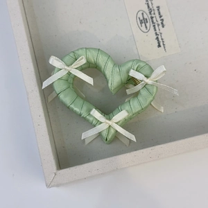 Detail view of light green silk ribbon heart hair claw with white bows on metal base