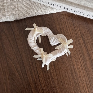 Détail de la pince à cheveux cœur en tissu crème avec nœuds en ruban sur du bois