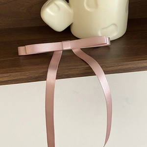 Detailed close-up of a pink satin ribbon bow hair clip on a textured wooden shelf