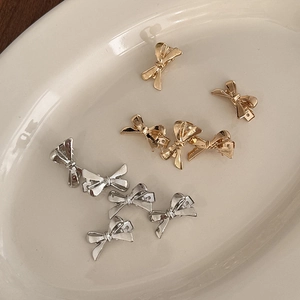 Nahaufnahme kleiner Metall-Haarklammern in Schleifenform in Gold und Silber auf einem Tablett