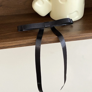 Close-up of black satin bow hair clip with long ribbons on a minimalist wooden shelf