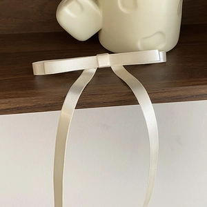 Detail of cream satin bow hair clip with long ribbons on a minimalist wooden shelf