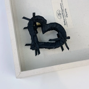 Detail of a black heart-shaped hair claw clip with satin ribbons and small bows