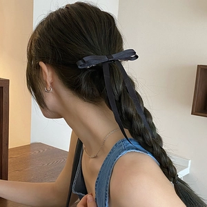 Elegant black silk bow hair clip with long ribbons styled on a braided hairstyle