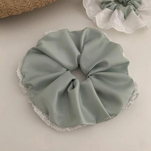 Détail d'un chouchou en soie vert sauge avec des bords en dentelle brodée blanche