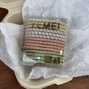 Detail of multi-color elastic woven hair ties with gold tinsel in a clear gift box
