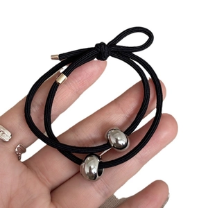 Elastic black hair ties with silver metal tube and bow detail shown on hand