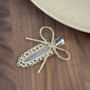 Barrette à cheveux avec nœud doré tressé et clip en métal argenté sur fond en bois