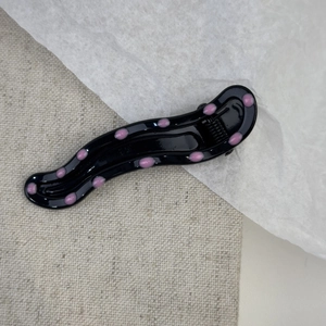 Pink polka dot wavy metal hair clip with black base on a textured fabric background