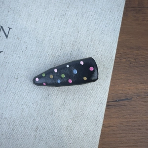 Détail d'une pince à cheveux noire avec pois colorés posée sur un livre en tissu
