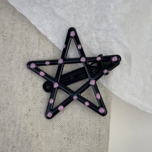 Detail of star-shaped metal hair clip with pink polka dots and matte black finish