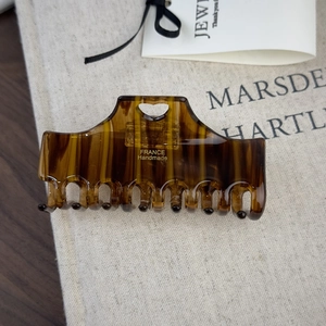 Detail of amber acetate hair claw with heart cutout and gold handmade logo on linen
