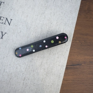Gros plan sur une barrette noire ornée de pois colorés en 3D sur fond texturé sobre