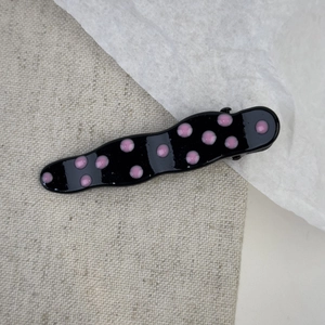 Detail of wavy metal hair clip featuring pink polka dots on a black finish base