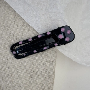 Close-up of a black rectangular BB hair clip with pink polka dots on a linen background