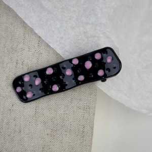 Close-up of pink polka dots on black rectangular metal hair clip with glossy finish