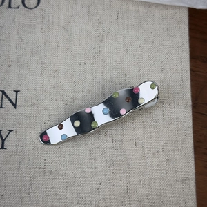 Barrette ondulée en métal argenté avec des pois colorés en émail sur fond beige clair