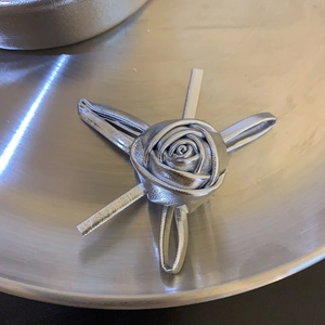 Makroaufnahme einer silbernen Rosen-Haarklammer mit metallischer Ledertextur auf Tablett