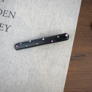Vue détaillée de la pince à cheveux noire à pois colorés sur un tissu texturé