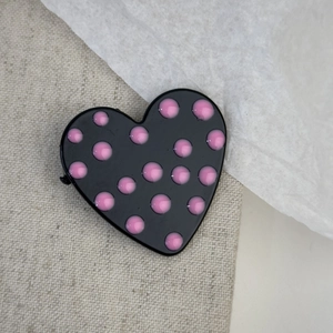Detailed view of a black heart hair clip with pink 3D polka dots on fabric background